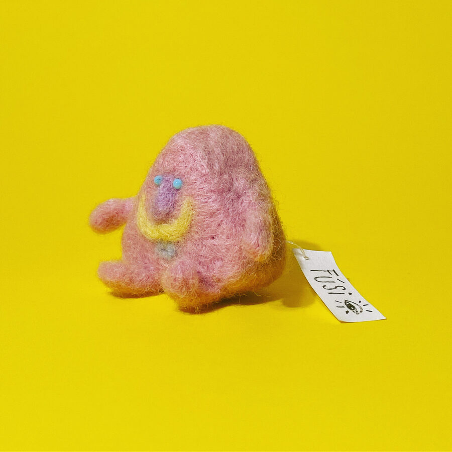 Needle felted pink moustache character on a yellow background.