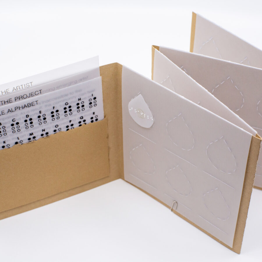 Image description: The open accordion book showing three information sheets printed on vellum tucked in a pocket. The other pages have embossed vellum slips with designated spots for the teardrop shapes to stay in. A line is embossed underneath to write out the Braille translation in English text.