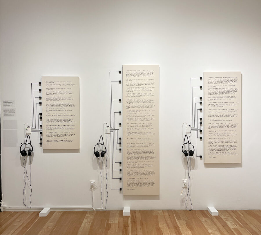 Image description: Three canvases with Braille painted on each are installed in a row. Each paragraph can be audio activated by touching the conductive paint connected to a touch board and headphones which are displayed next to each canvas.