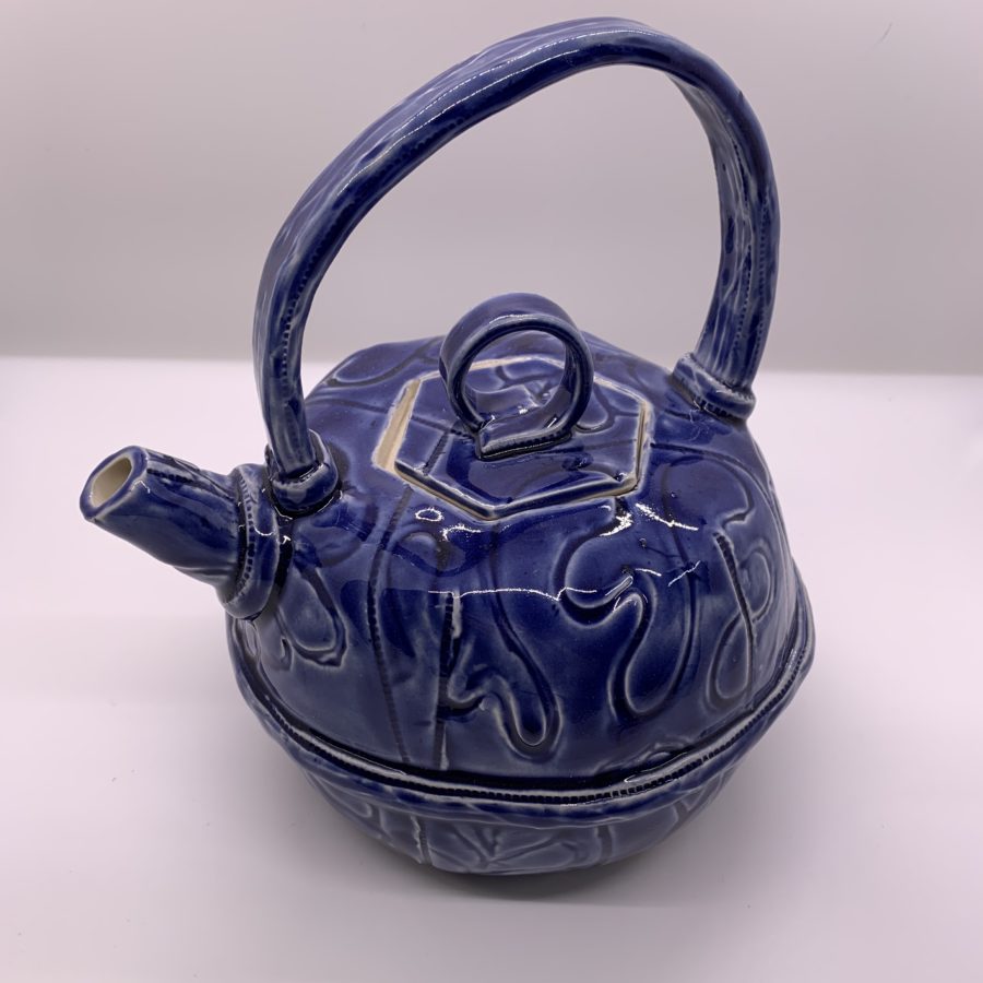 Blue glaze hand built teapot made from two slab-built bowls combined together with a “belt” of clay around the middle seam, and a handle over the top of the pot from the spout to the back of the lid