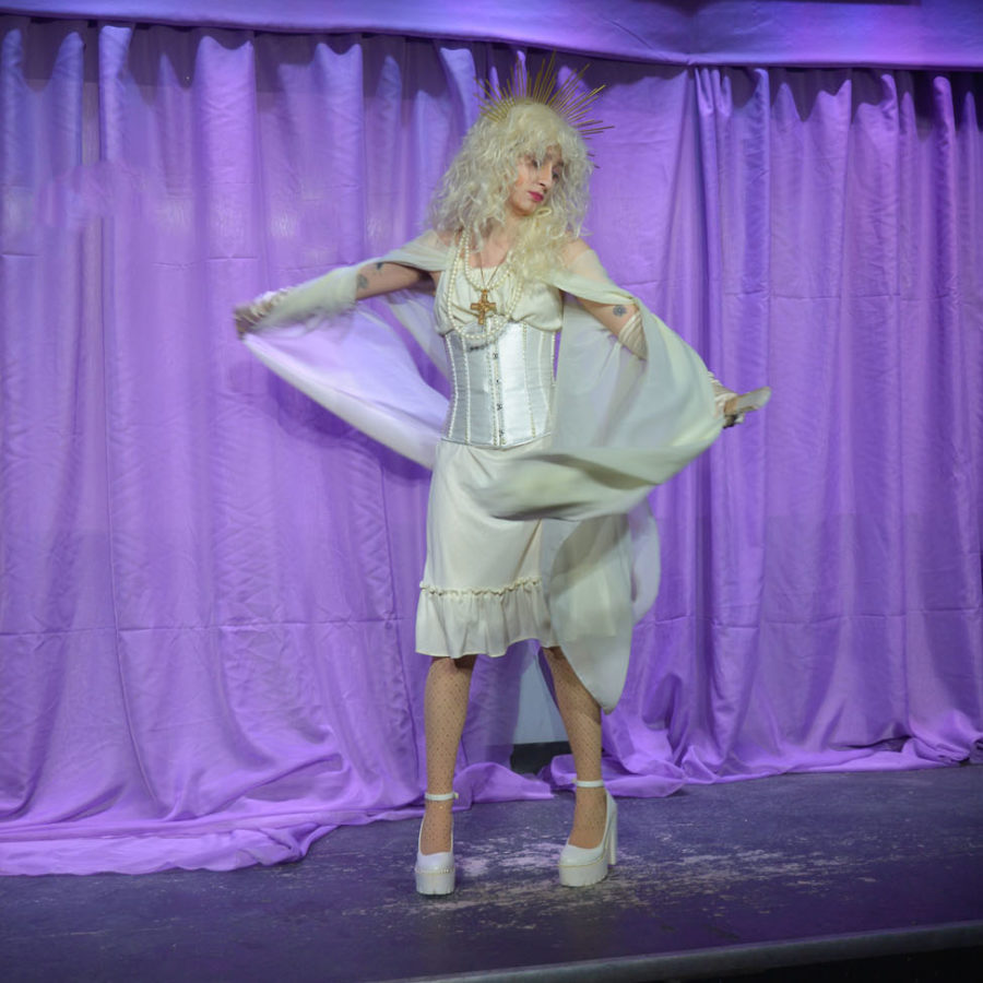 St. John Boy on stage at The Well. He is wearing all white and spinning with white fabric twirling around him. The stage is lit up purple. 