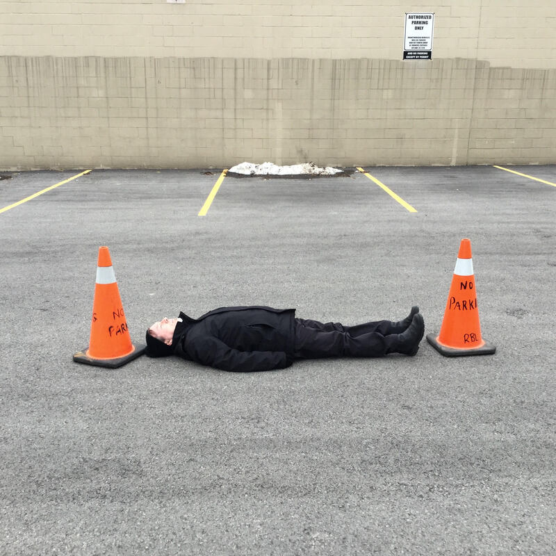 Safety Performance, 2018, A figure lies on the ground between two orange safety cones