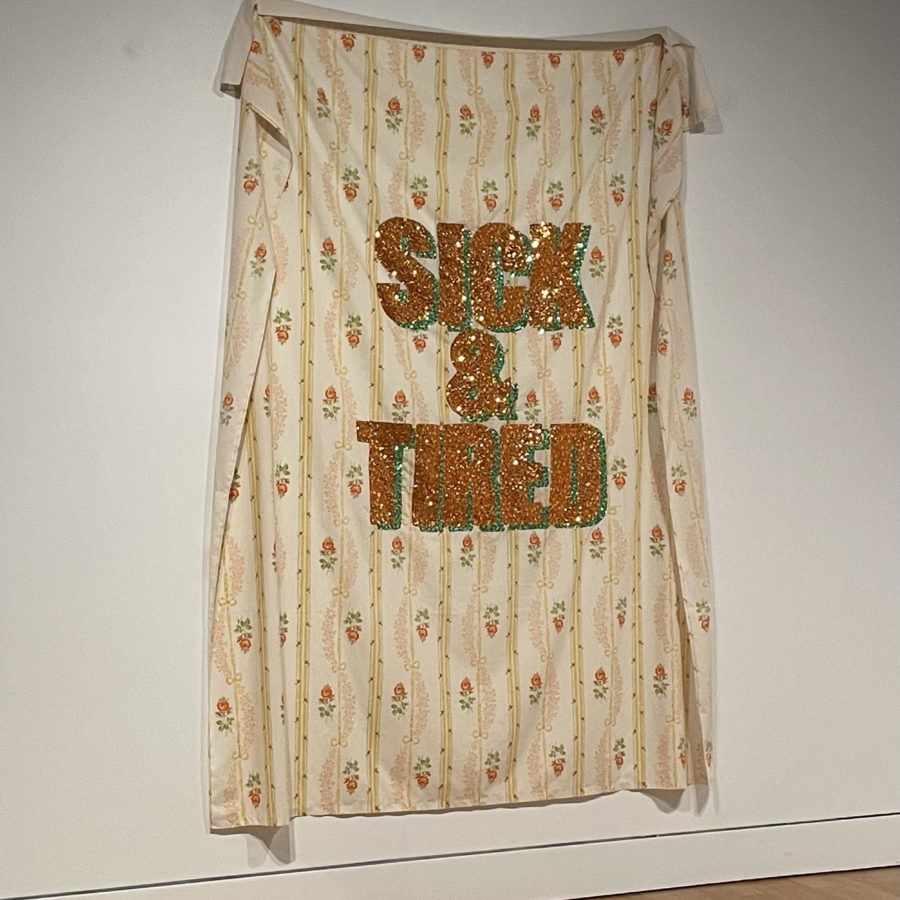 SICK & TIRED, sequins on bedsheet, 2017, Permanant Collection of the Art Gallery of Hamilton, an orange patterned sheet with the words sick & tired in orange and green sequins