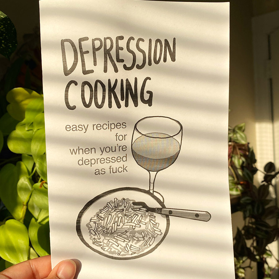 A hand holds up a black and white zine against a backdrop of a sunny room filled with plants. The zine reads: Depression Cooking, easy recipes for when you're depressed as fuck