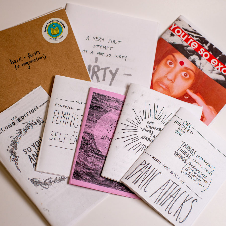 A collection of many various zines spread across a white table.