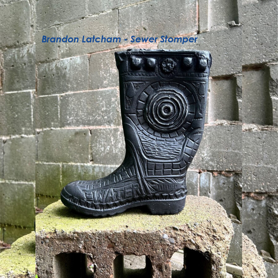 Cast iron sculpture of a rubber boot with raised and receded patterns, sitting on cinder block. By Brandon Latcham
