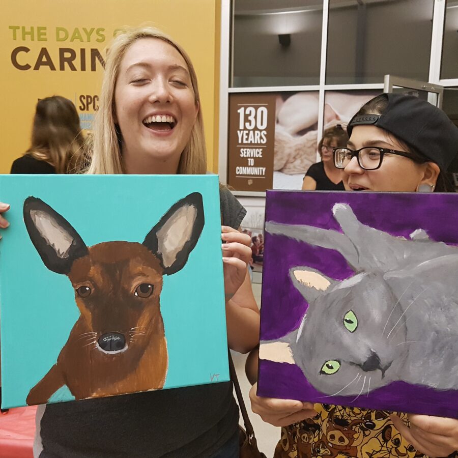 Two women showing off their completed pet paintings.