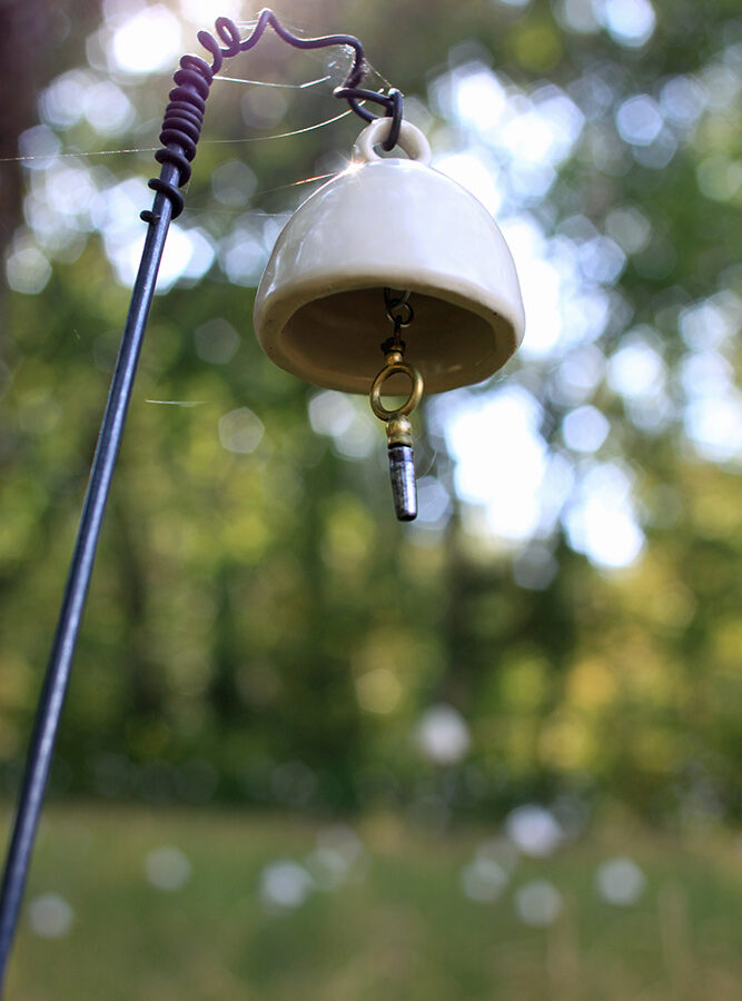 Detail image of a single bell from jardin de l'empereur, 2012. The bell is ceramic with a key found on site as the ringer, hanging off of a piece of piano wire, the wire is 36