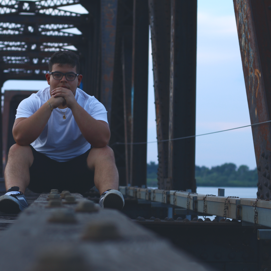 Young man sitting on the train tracks over a river.