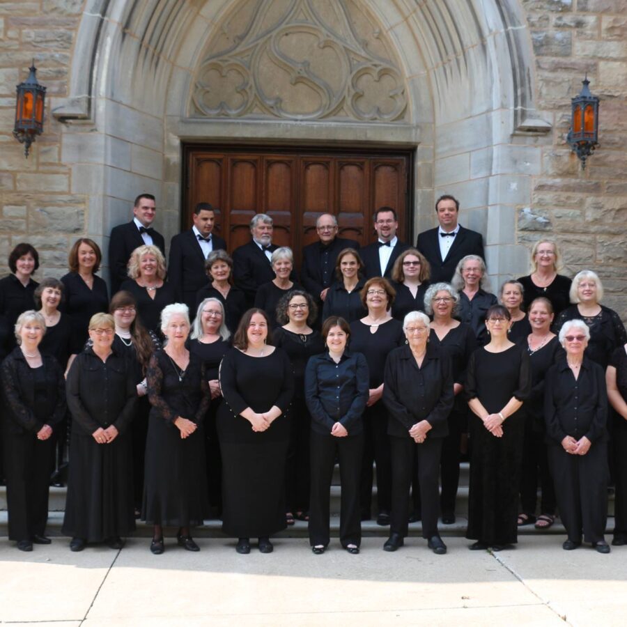 Choir members dressed in formal black dresses and suits posed in front of wooden door of a church