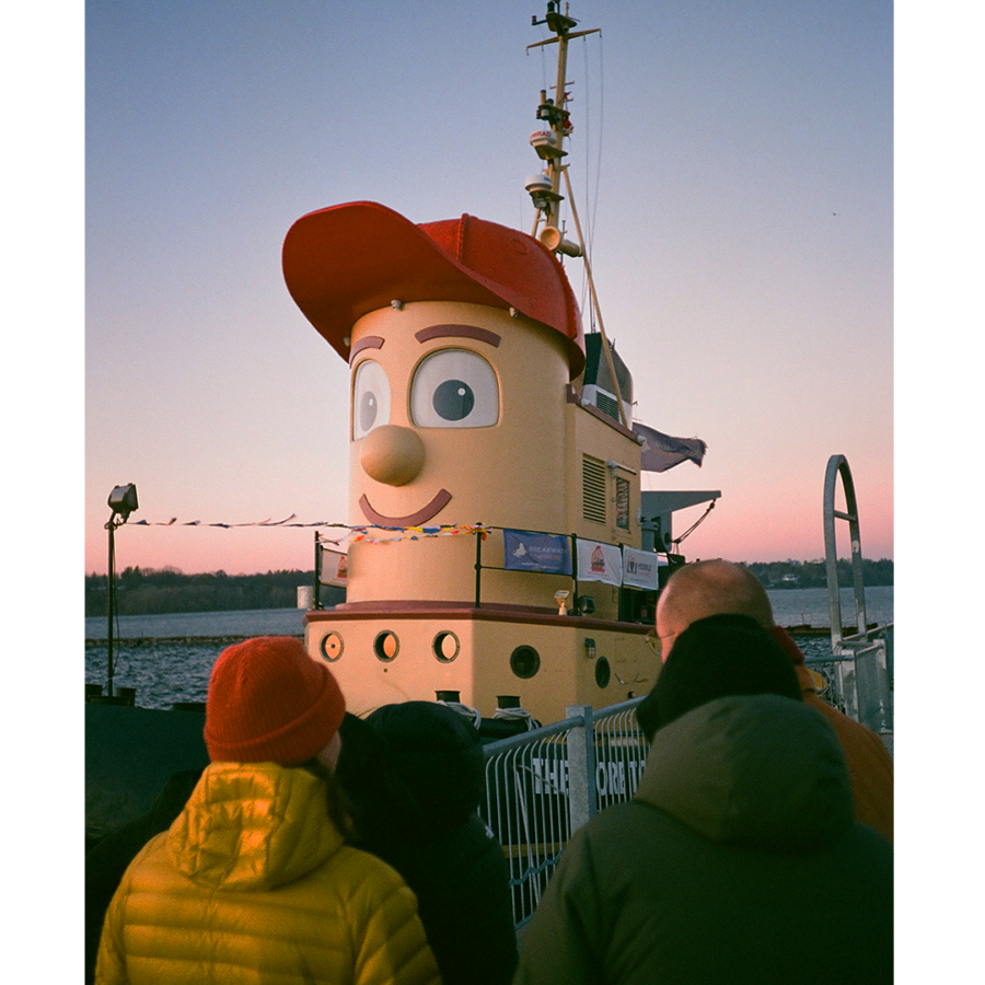 A photograph of 4 people looking at the tugboat Theodore, Too docked in Hamilton Habrour.